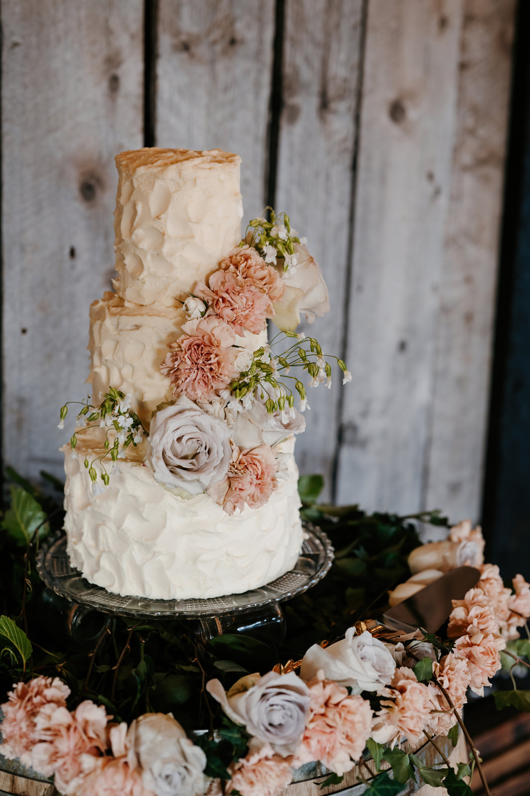Yeraldy's wedding cake — three-tier white buttercream with peach florals on weathered wood